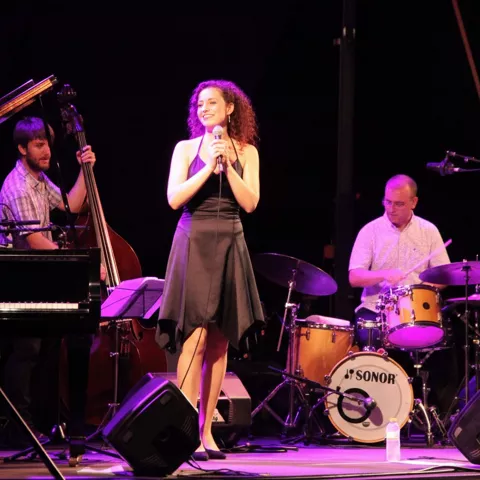 Cantante acompañada por piano, contrabajo y batería en concierto nocturno.