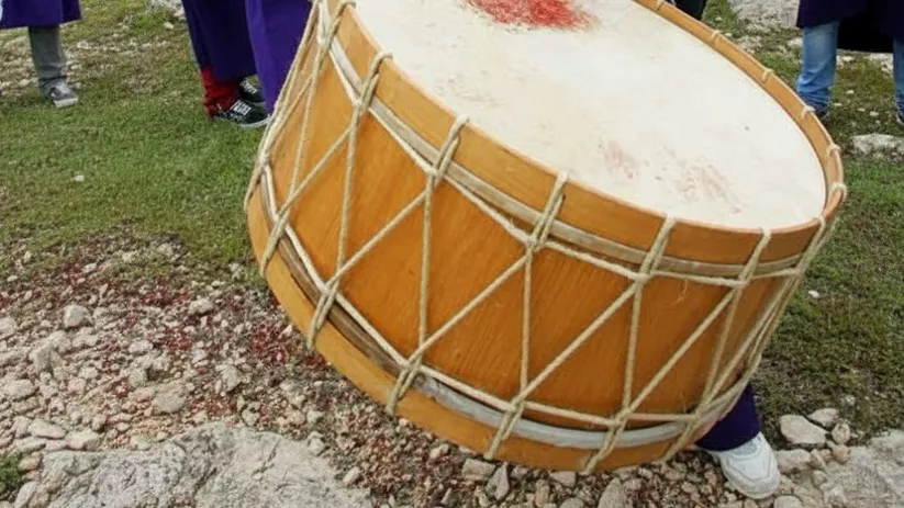 Jóvenes con túnicas moradas tocan tambores en colina al aire libre.