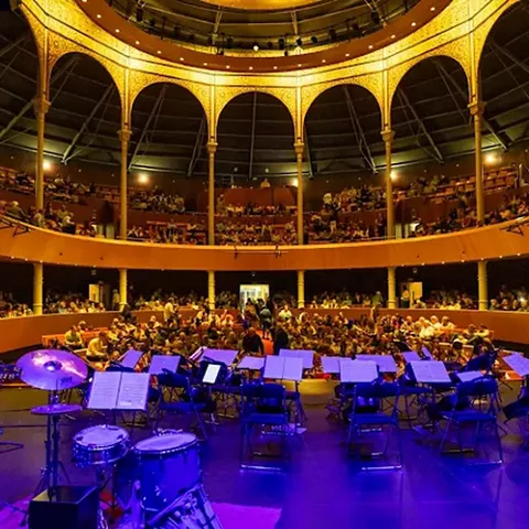 Escenario con orquesta preparada frente a un auditorio lleno de espectadores.