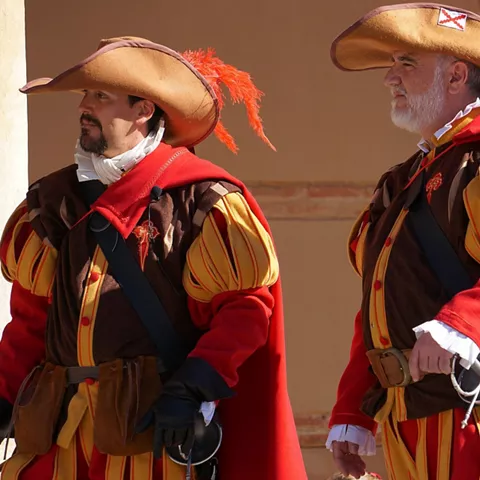 Hombres con uniformes históricos y sombreros emplumados.