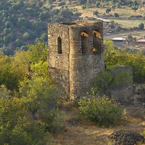 Torre de piedra en lo alto de una colina rodeada de vegetación y restos murarios.