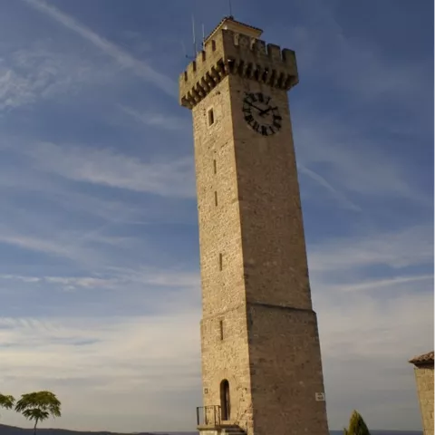 Torre de piedra con reloj en mirador urbano y cielo despejado.