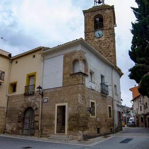 Iglesia de piedra con torre del reloj vista desde una calle estrecha.