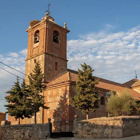 Iglesia de ladrillo con torre campanario y muro perimetral de piedra