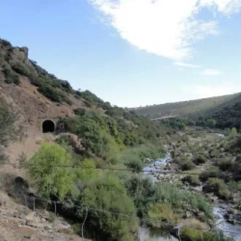 Sendero junto a río con túnel al fondo del valle