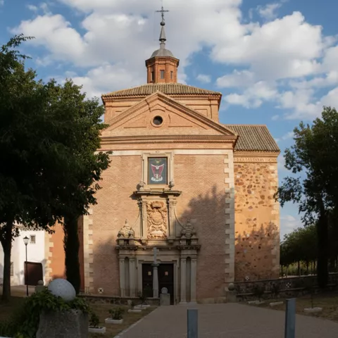Vista frontal de la fachada de una iglesia de ladrillo con una entrada barroca ornamentada de piedra, un escudo tallado y una pequeña cúpula con linterna.