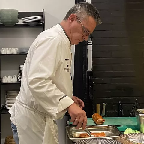 Cocinero prepara un plato en una cocina con bandejas y una botella