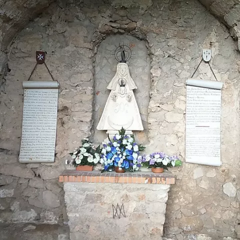 Imagen religiosa en hornacina de piedra con ofrendas florales