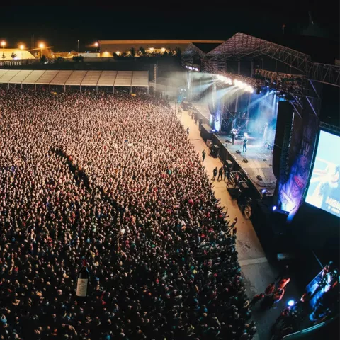 Vista aérea de un concierto nocturno con un mar de asistentes frente al escenario.