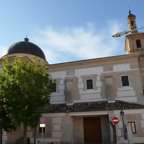Una vista exterior de una gran iglesia con un muro texturizado de bloques claros y oscuros, una gran cúpula y una torre de ladrillo.