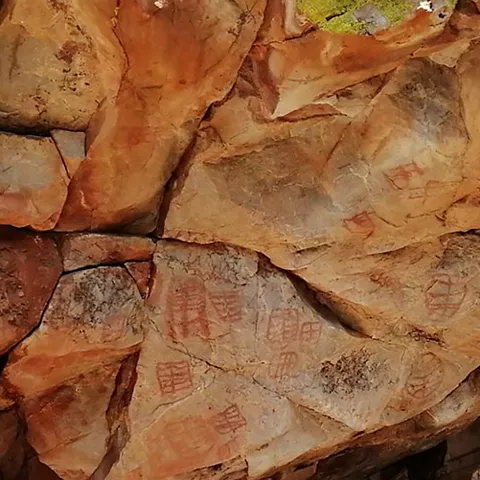 Primer plano de pared rocosa con pinturas rupestres geométricas en tono rojizo.