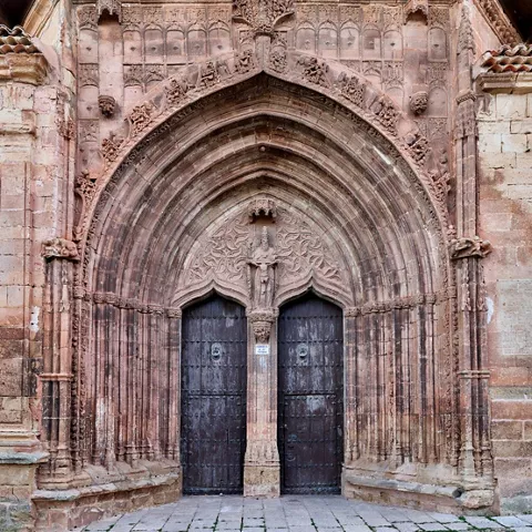 Detalle de portada gótica tallada en piedra con puertas de madera.