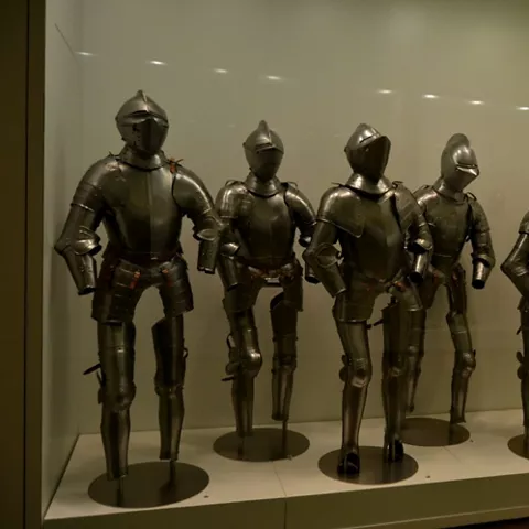 Exposición de armaduras metálicas alineadas en una vitrina de museo.