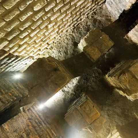 Vista inferior de pilares de piedra y bóvedas de ladrillo con iluminación puntual.