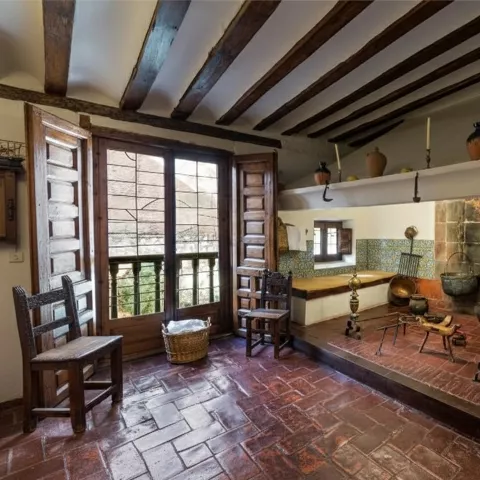 Cocina tradicional con chimenea, utensilios antiguos y vigas de madera en el techo.