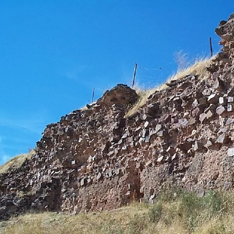 Muralla de piedra en ruinas sobre ladera seca bajo cielo despejado.