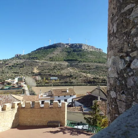 Vista elevada de un pueblo con muralla y montaña al fondo.
