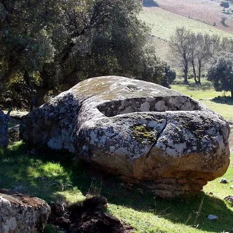 Gran roca tallada en pradera con árboles y paisaje ondulado.