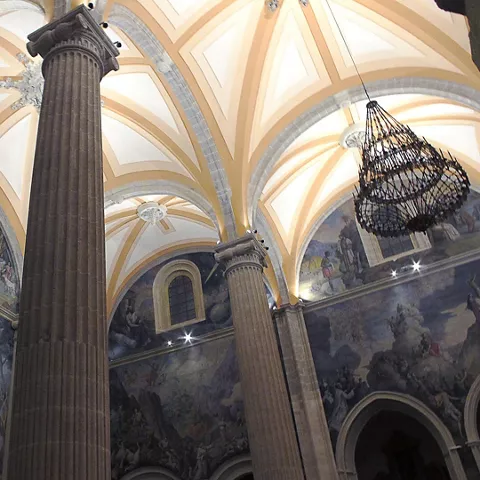 Interior de iglesia con columnas altas, bóvedas decoradas y pinturas murales.