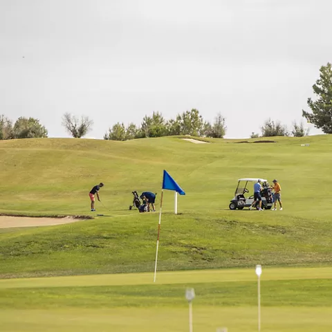 Vista panorámica del campo con jugadores, banderas y colinas verdes.