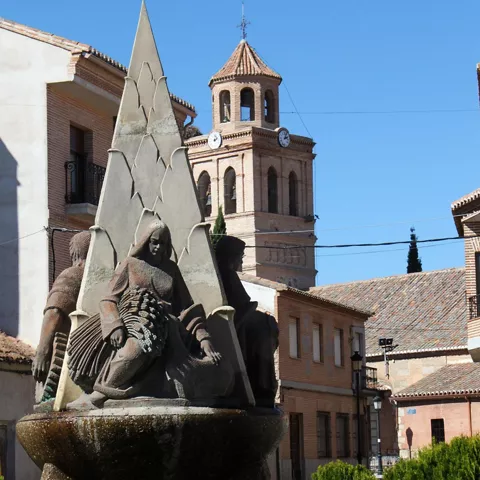 Fuente escultórica con figuras y campanario detrás