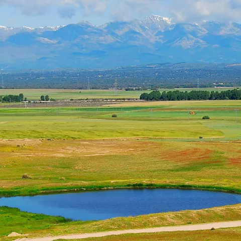 Llanura verde con laguna y montañas al fondo