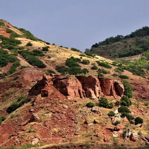 Ladera de tonos rojizos con formaciones rocosas y vegetación dispersa