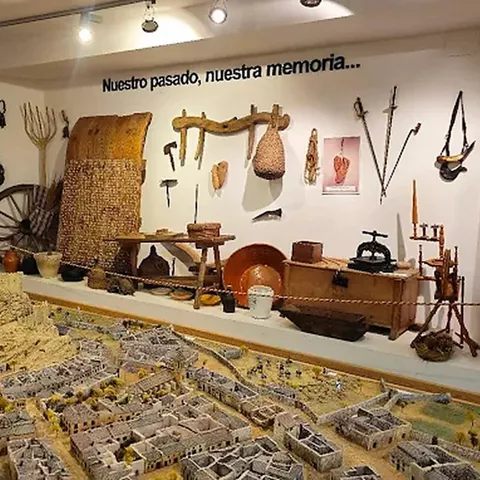 Maqueta urbana detallada acompañada de herramientas y objetos tradicionales expuestos en la pared.