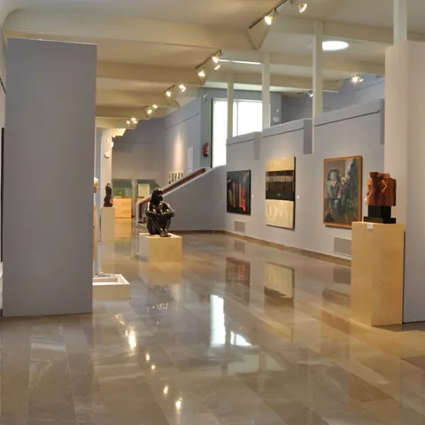 Sala de exposiciones con esculturas y cuadros dispuestos en un espacio amplio.