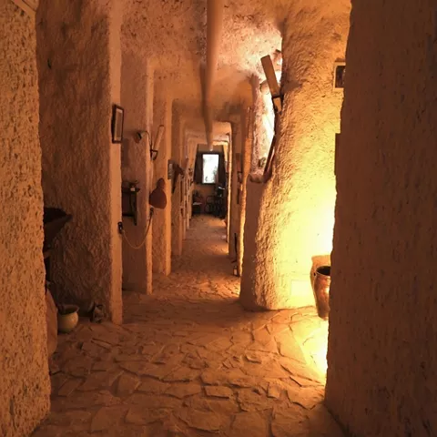 Pasillo interior excavado en roca con iluminación cálida y suelo empedrado.