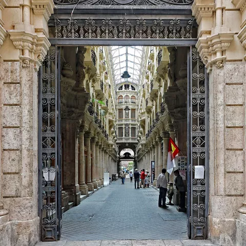 Entrada monumental con reja de hierro que da paso a una galería histórica con columnas.