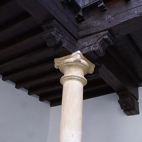 Detalle arquitectónico de columna de piedra y vigas de madera en techo interior.