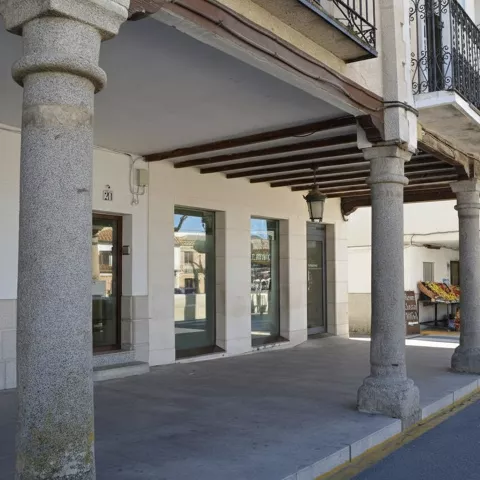 Soportales con columnas de piedra y balcones sobre calle tranquila.