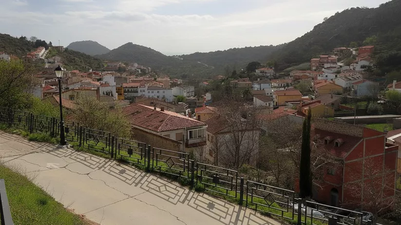 Una calle residencial que serpentea por un pueblo en una colina, con tejados de terracota y vistas a las montañas al fondo.