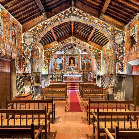 Interior de templo con bancos de madera y murales pintados.