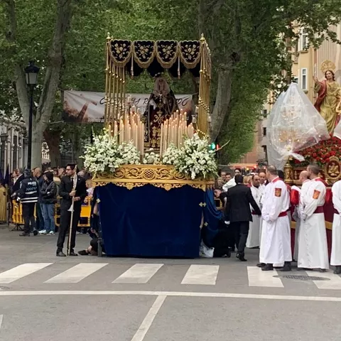 Procesión con paso religioso y participantes con túnicas en avenida urbana.