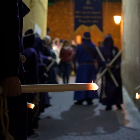Personas con túnicas sosteniendo velas encendidas en una procesión nocturna.