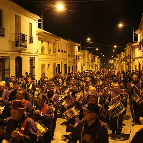 Procesión nocturna con numerosos tamborileros iluminados por farolas.