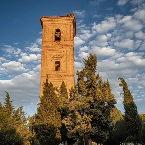 Torre campanario de ladrillo al atardecer con escalinata y cipreses.