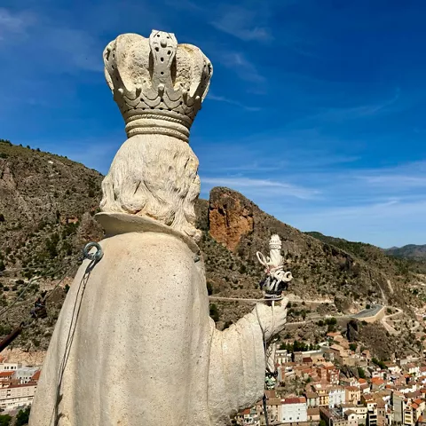 Escultura de piedra vista desde atrás dominando un pueblo entre montañas