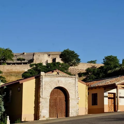 Edificio de acceso con arco de piedra junto a muralla sobre colina