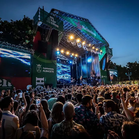 Gran escenario nocturno con luces intensas y multitud siguiendo la actuación desde la plaza.