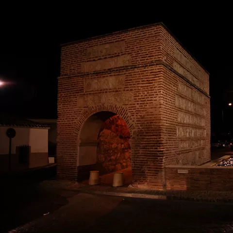 Arco iluminado de noche junto a una fuente.