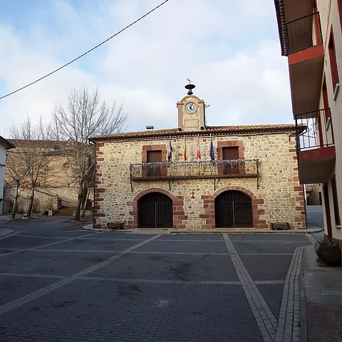 Plaza tranquila con edificio institucional de piedra y torre con reloj.