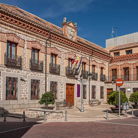 Edificio histórico de piedra y ladrillo con balcones y plaza urbana