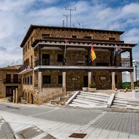 Edificio institucional de piedra con soportal, escalinata y banderas.