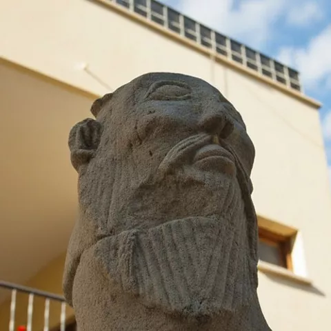 Escultura de piedra con forma animal vista en primer plano junto a un edificio.