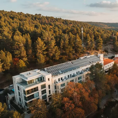 Vista aérea de un hotel entre bosques, con tejados rojos y colinas al fondo.
