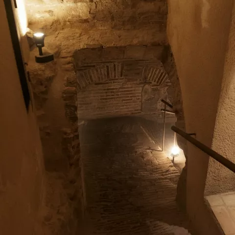 Escalera descendente hacia pasillo subterráneo con bóveda de ladrillo.