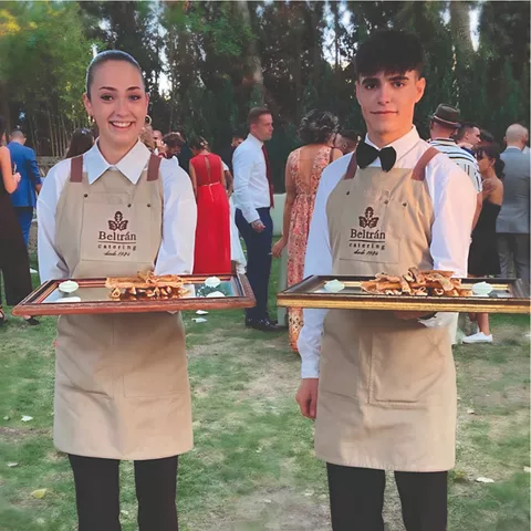 Dos camareros con bandejas en una celebración al aire libre